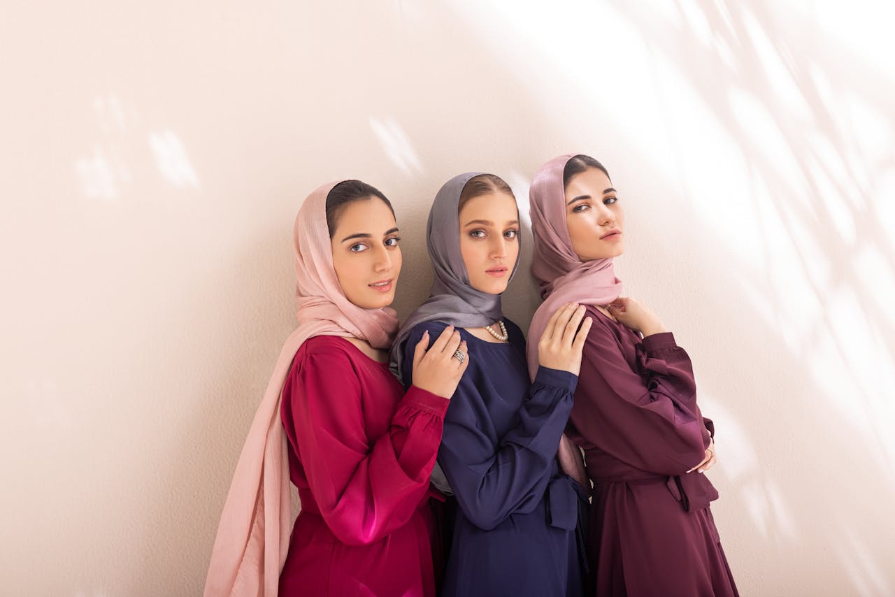 Three women elegantly pose in stylish hijabs against a light backdrop.